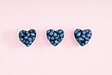 Fototapeta premium Plate in shape of heart with blueberries on pastel pink background. Blueberry berries background. Valentine's Day. Flat lay, top view, copy space