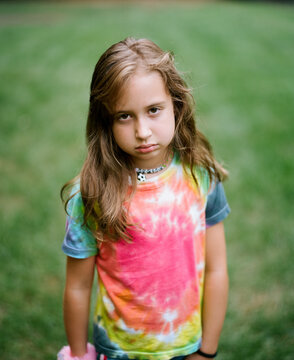 Portrait of a cute young girl in a tie-dye shirt with a grumpy expression