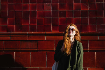 Portrait of young woman with red hair against red tile wall