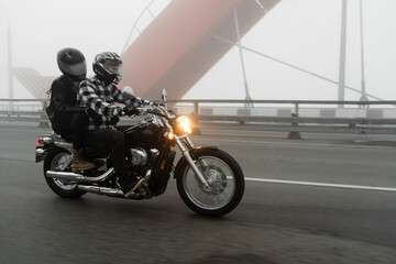 Attractive couple riding vintage motorcycle across the bridge over river, foggy weather.