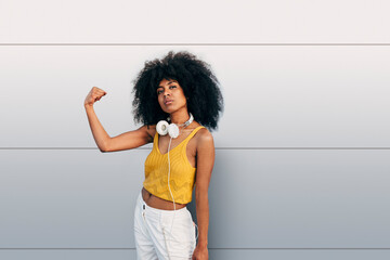 Afro woman looking at camera besides a grey wall
