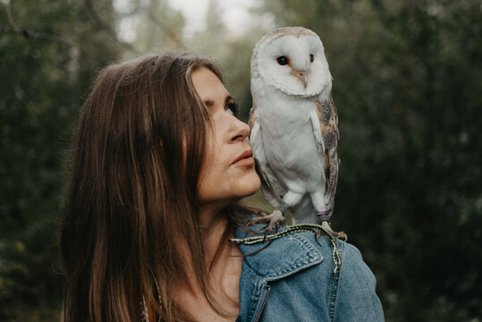 A woman in her twenties posing for a portrait with an owl in a forest