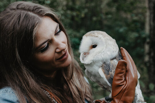 A woman in her twenties posing for a portrait with an owl in a forest