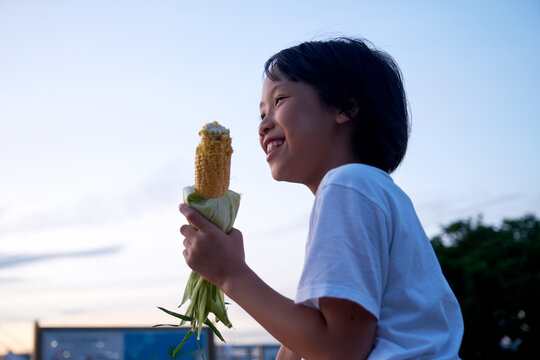 Asian little girl eating corn. Tokyo seaside at sunset