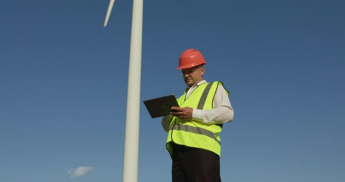 Young male engineer looking at wind turbine statistics environmental energy energy windmill field worker renewable slow motion