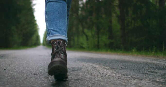 Slow-motion convert close-up, you traveler shoes are walking down the road in jeans. Shoes go on a forest path on the asphalt