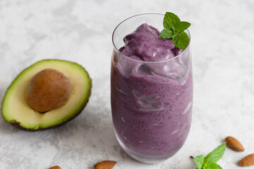 Summer refreshing smoothie with avocado, blueberries and almond milk in a glass glass on a light background. Diet cocktail, keto recipes.