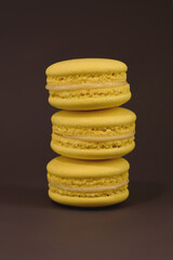 Three tasty yellow macarons on the brown background.