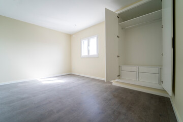 Fototapeta premium Empty room with dark wooden floating laminate flooring and wardrobe. House interior, wide bedroom space. Newly recently painted new apartment or house. Wood floor. Real state and property management