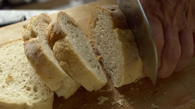 Slicing crunchy bread with a knife on a wooden cutting board..A wheat-flour&nbsp;fresh crispy white bread.  Close up.