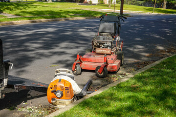 Large professional lawn mower and leaf blower in the street by a curb near a a trailer