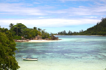 Beautiful wild bay on Seychelles island, with a boat in turquoise blue water sea and white dans beach, granit rocks and green vegetation.