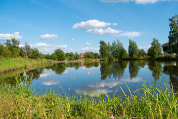 Fototapeta na wymiar Lake in the village. The sky is reflected in the water. Summer