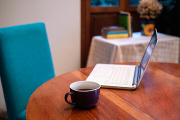 a laptop and a cup of coffee over a wooden table, books on the background 