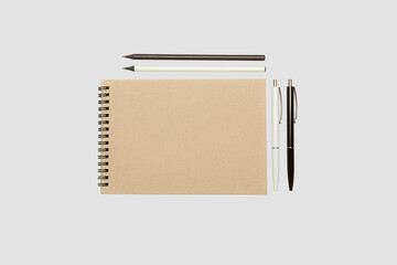Blank spiral notepad mockup template with kraft paper cover with black and  white pens isolated on light gray background.