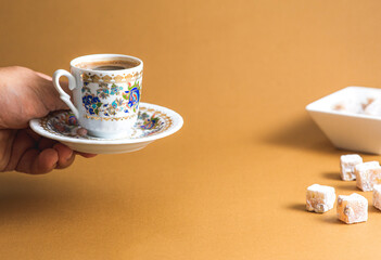 An anonymous hand is serving Turkish coffee and Turkish delight view over mono color minimal brown...