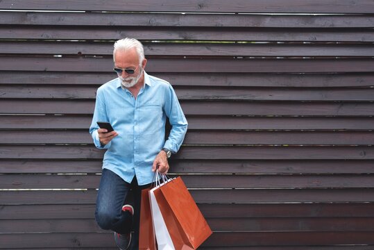 Senior man using mobile phone and holding shopping bags
