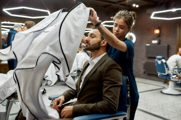 Handsome man in barbershop. Professional barber girl or hairdresser serving client