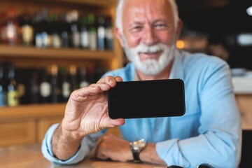 Senior man showing mobile phone at restaurant
