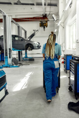 African american woman, professional female mechanic in uniform pulling, carrying tool box cart in auto repair shop. Car service, maintenance and people concept