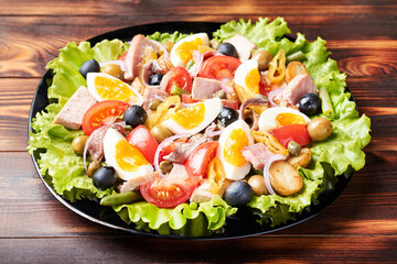 A large platter of tuna salad (nicoise) stands on a wooden table.
