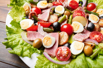 A large platter of tuna salad (nicoise) stands on a wooden table.