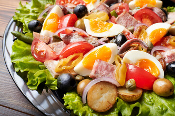 A large platter of tuna salad (nicoise) stands on a wooden table.
