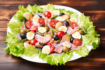 A large platter of tuna salad (nicoise) stands on a wooden table.