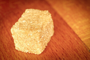 A cube of soluble brown sugar lies against a background of wood. Brown sugar is more healthy.