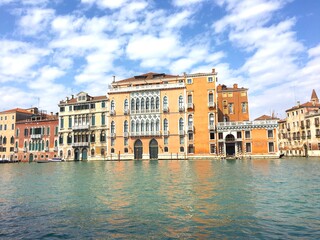Beautiful view of a venician palace  on a venetian canal with red ocre, orange and yellow building facade, Venice, Italy.
