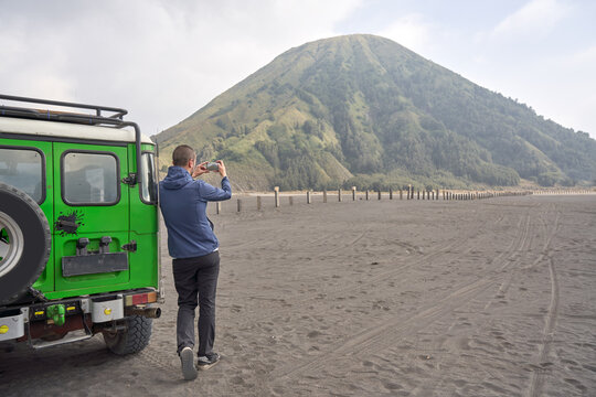 Man visiting Bromo volcano, Leaning To a jeep and using a mobile phone.