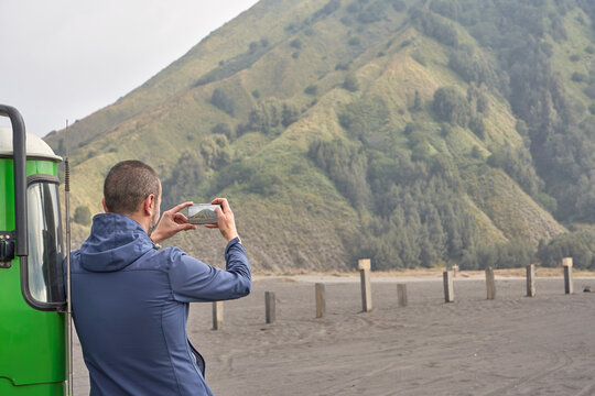 Man visiting Bromo volcano, Leaning To a jeep and using a mobile phone.