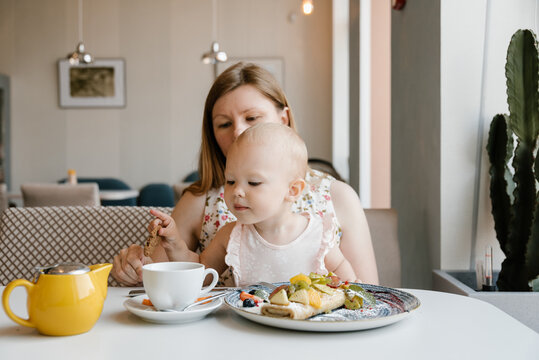 Cute baby girl having breakfast with mother in cafe.