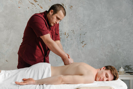 Masseur in red suite presses with fist on clients back.