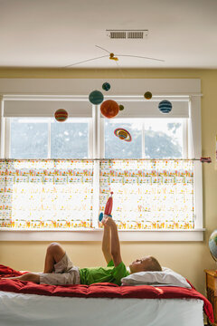 Child Astronaut Lying on Bed with Toy Rocket Ship and Solar System Mobile