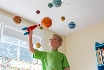 Future Astronaut Playing with Toy Rocket Ship and Solar System Mobile