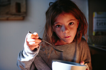 little girl eats cereal for breakfast in morning sun