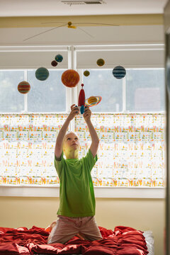 Child Astronaut Playing with Toy Rocket Ship and Solar System Mobile