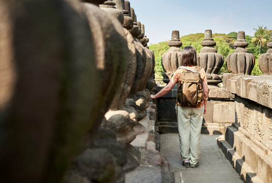 Back view of woman with backpack looking at a hindu carving in Prambanan Temple, Java, Indonesia