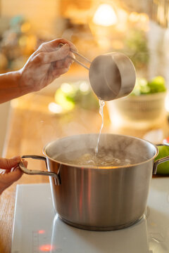 Housewife pouring water into boiling pot
