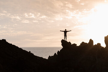 Silhouette of male standing on rocky bridge and rising up.