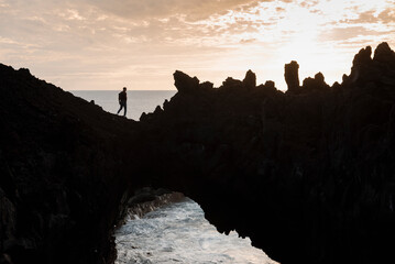Silhouette of man going natural arch from stones.