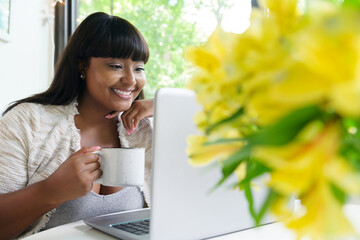 Woman holding cup of coffee, looking at laptop