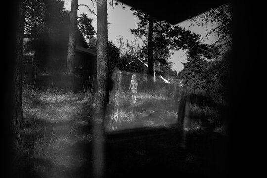 Little girl exploring in woodland seen through a cabin window.