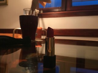Red open lipstick displayed on modern glass table in dimmed light room with wood window frame background 