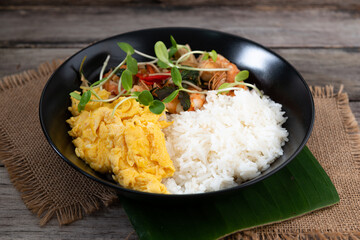 Rice topped with stir-fried shrimp and basil, and fried eggs in white dish.