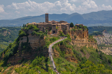 Fototapeta premium Tourists walk along a small bridge to get to the beautiful medieval hill town of Civita di Bagnoregio, located in the Tuscany region of Italy.