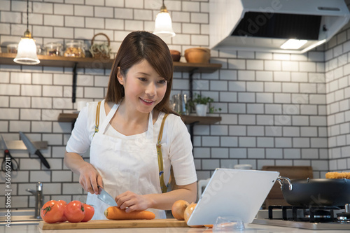 タブレットpcを見ながら料理する女性 Wall Mural Wallpaper Murals Paylessimages