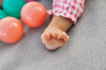 Fototapeta na wymiar Tiny baby girl foot on a gray background with plastic balls, childhood and active kids concep