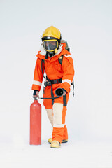 Fototapeta premium A portrait of Asian male firefighter in red protective uniform, mask and helmet with fire extinguisher standing on white background.